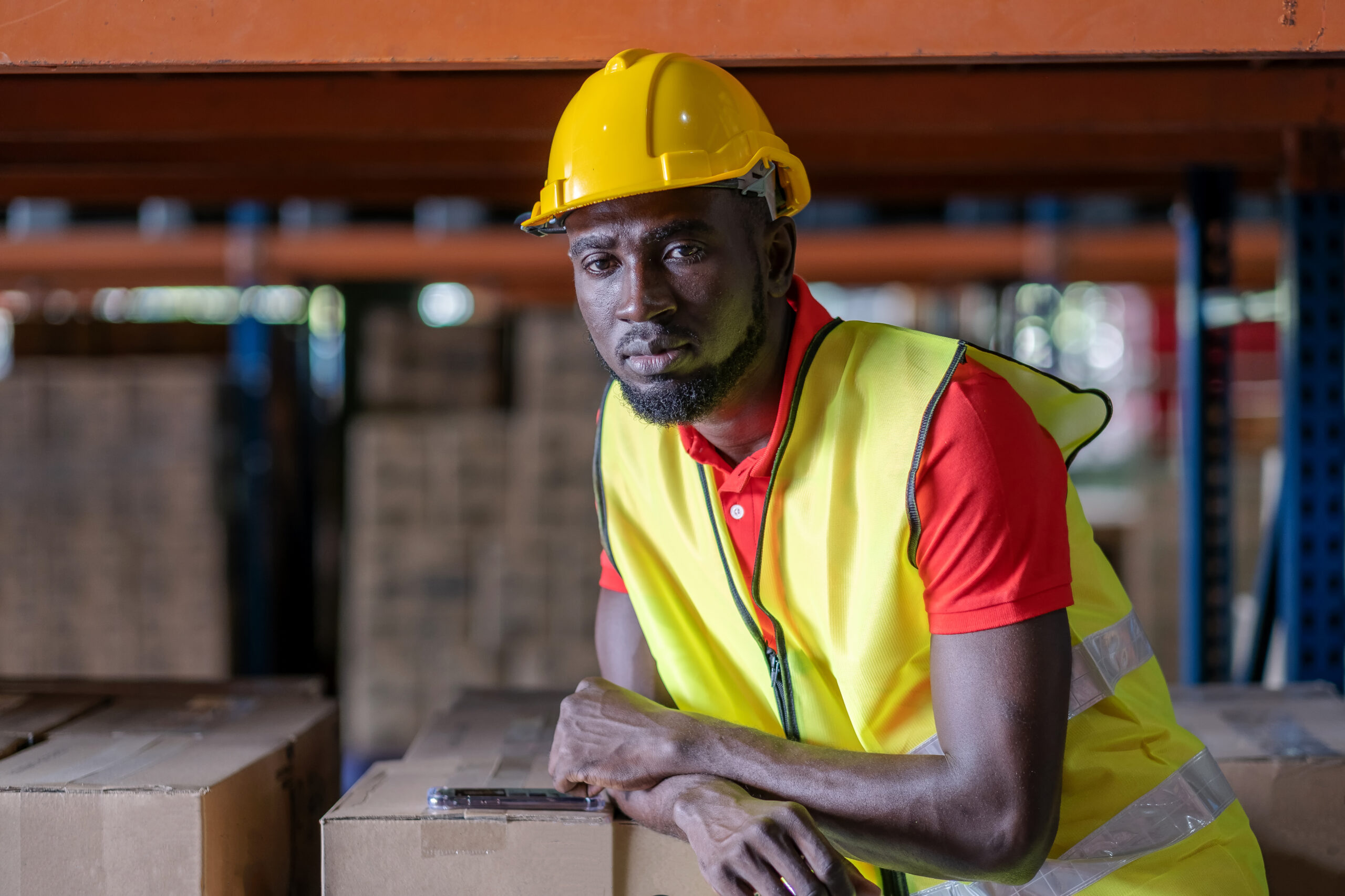 Africa American engineer man wearing safety helmet and vest standing in the automotive part warehouse. Looking at camera Portrait of worker. Logistic and business export at distribution center